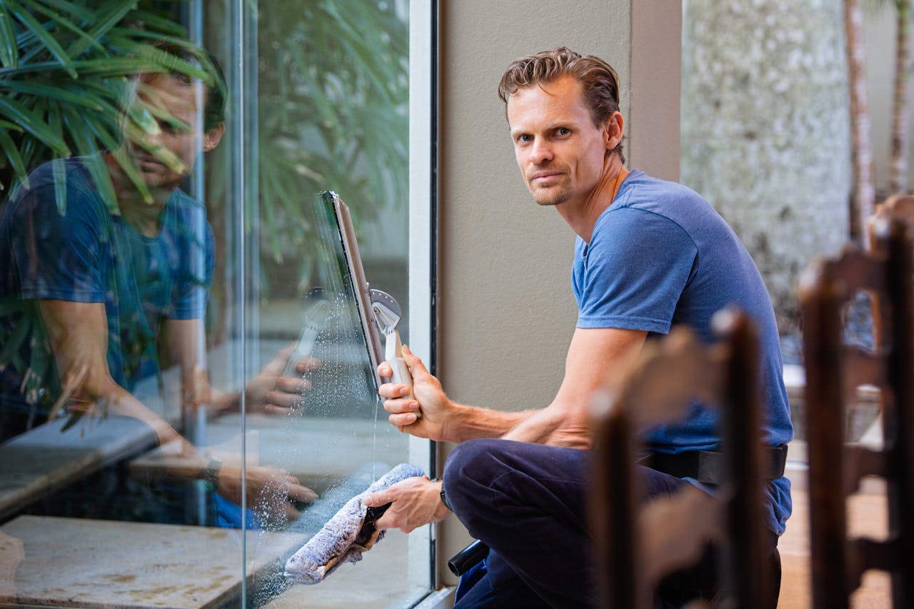 pexels-photo-634007 A man in a blue t-shirt cleaning large glass pane with a squeegee indoors.